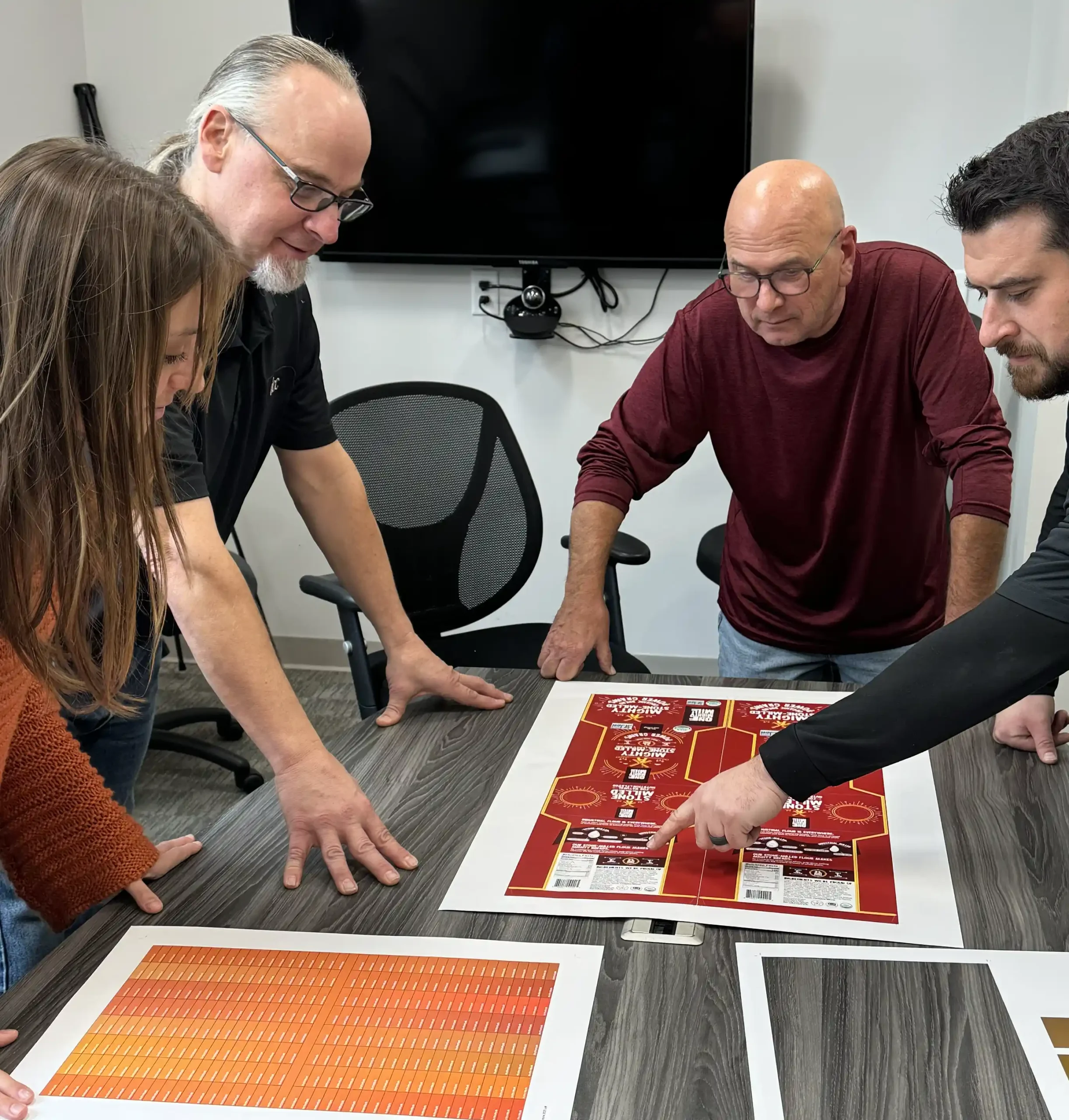 men and women standing at a table reviewing a press sheet