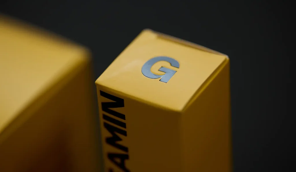Close-up of a yellow product packaging box with a metallic letter ‘G’ on top and the word ‘GLEAMIN’ printed vertically on the side.