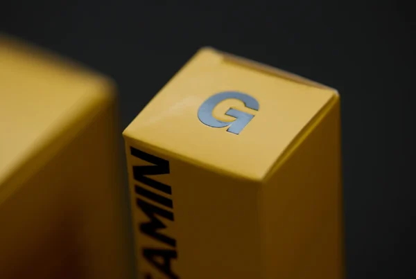 Close-up of a yellow product packaging box with a metallic letter ‘G’ on top and the word ‘GLEAMIN’ printed vertically on the side.