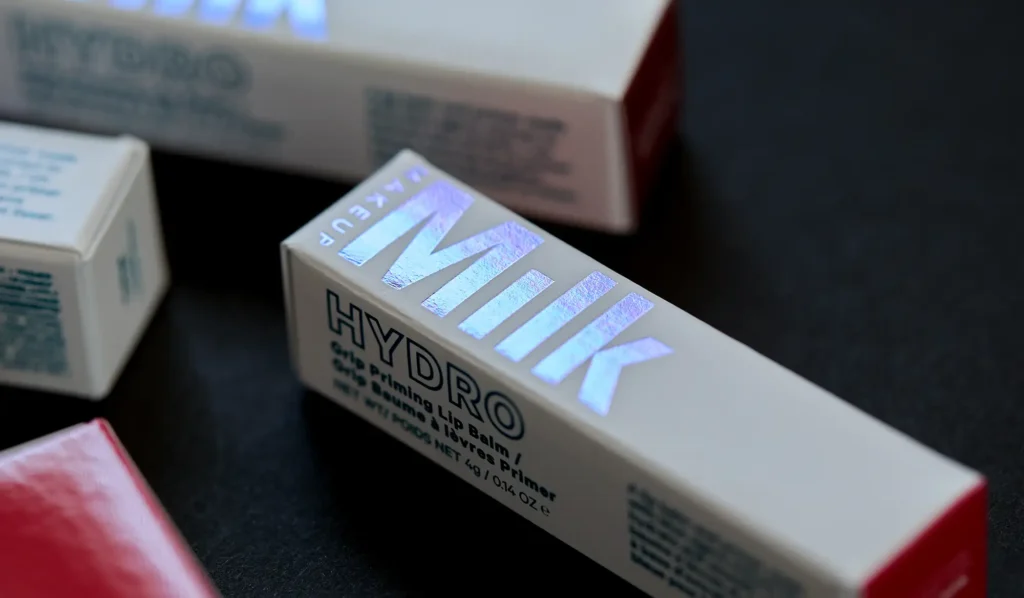 Close-up of Milk Makeup Hydro Grip Priming Lip Balm packaging with iridescent holographic lettering on a light-colored box.