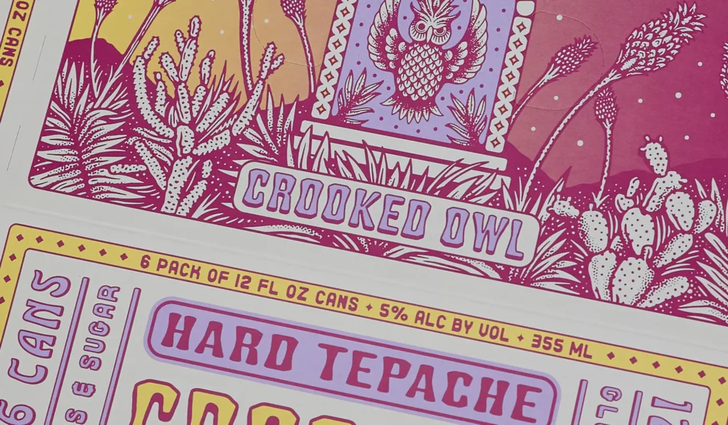 Colorful illustrated packaging for Crooked Owl Hard Tepache, featuring a stylized owl surrounded by desert plants in pink, purple, and yellow tones.