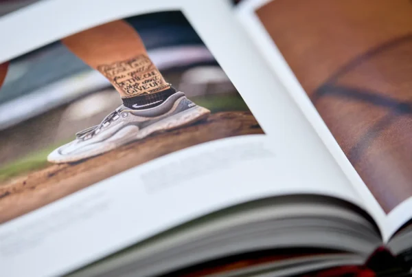 Close-up of an open photo book showing a picture of an athlete's lower legs wearing running shoes and socks with motivational text, standing on a dirt surface.